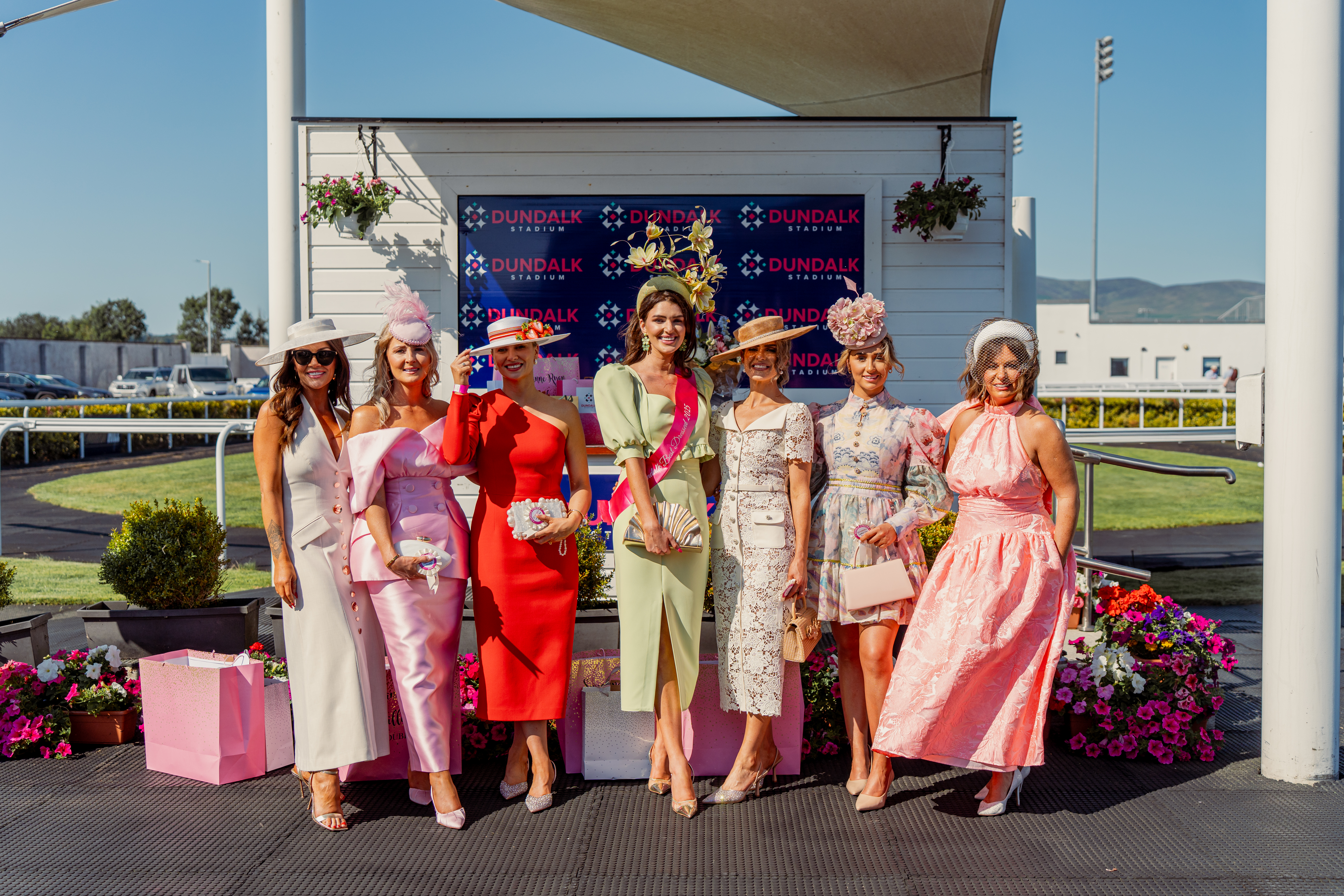 This is an image of three incredibly dressed women standing outside Dundalk Stadium on a sunny day. These women are the 2026 Ladies Day runners up, judges and winner