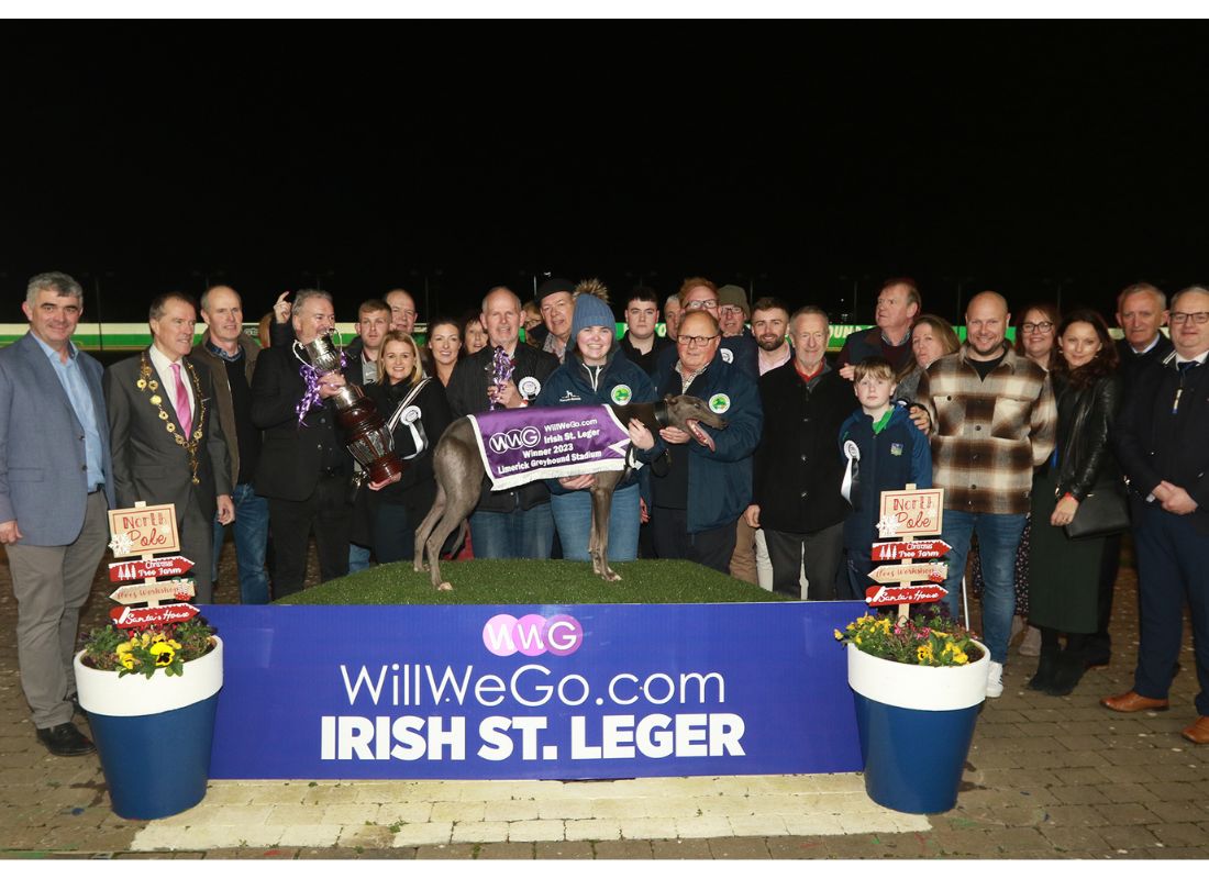 Image shows a large group of people at the winner's podium of Limerick Greyhound Stadium for the presentation by WillWeGo.com's Ray Quinn to winning owners James and Muireann Murphy, trainer Graham Holland, Breeder Jerry Murphy and winning greyhound Clonbrien Treaty. The group includes a number of people including the Mayor of Limerick and TD's and Councillors and connections of the 2023 WillWeGo.com Irish St Leger Final 