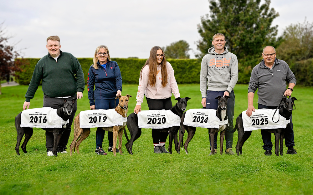Image shows 5 people holding 5 greyhounds in a green field area with a hedge behind them. The Holland Family pictured at their Tipperary home in Riverside Kennels with their record breaking 5 Irish Greyhound Derby winners. Chris with 2016 champion, Rural Hawaii, Nicky with 2019 champion Lenson Bocko, Rachel with 2020 champion Newinn Taylor, Timmy with 2024 champion Bockos Diamond and Graham with 2025 champion Cheap Sandwiches. Pic courtesy of Greyhound Racing Ireland